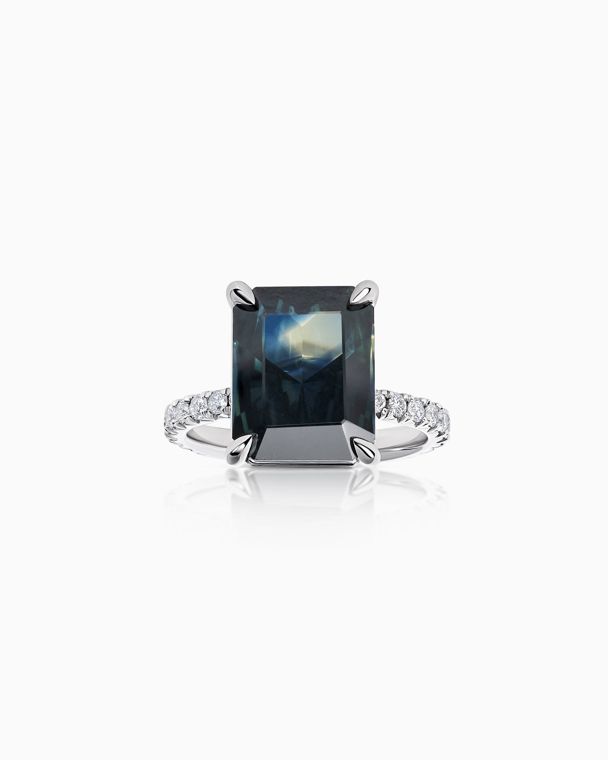 18k white gold ring featuring a large emerald-cut teal parti sapphire in a four-claw setting, with fishtail-set round brilliant diamonds on the shoulders, photographed on a white background.