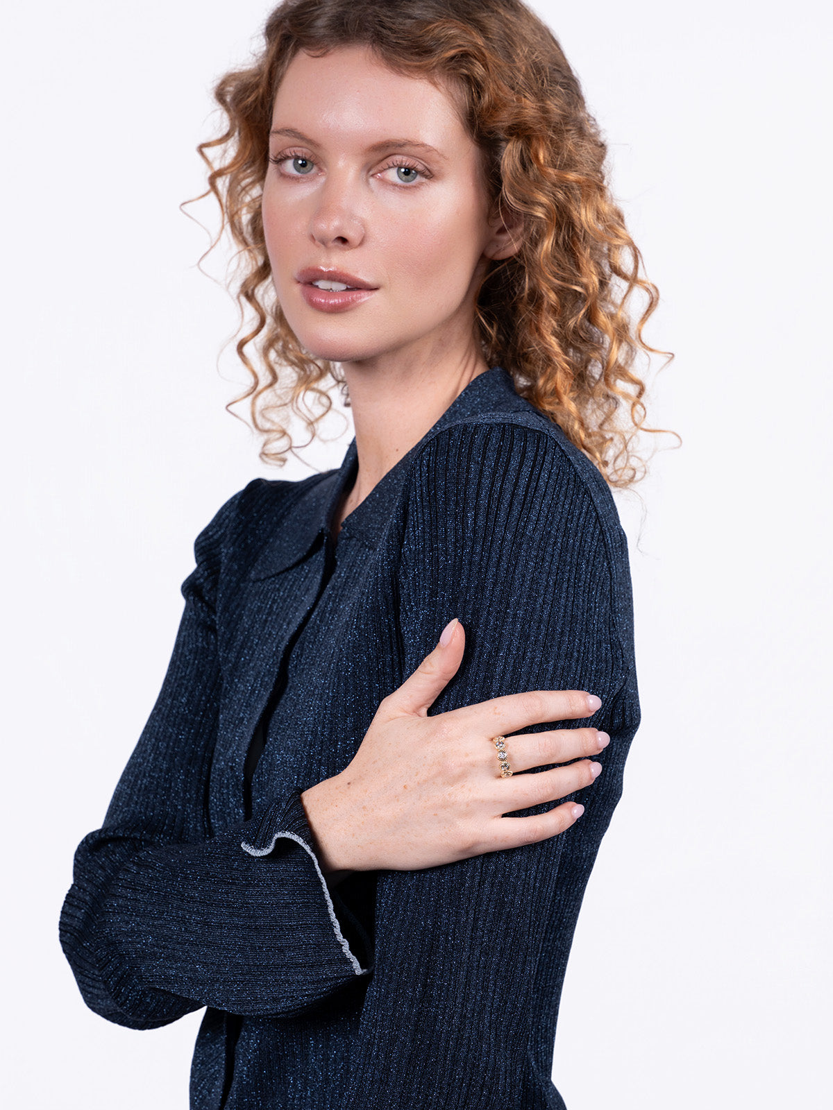 A woman with curly light brown hair wearing a dark navy ribbed knit cardigan, posed against a solid white studio background.