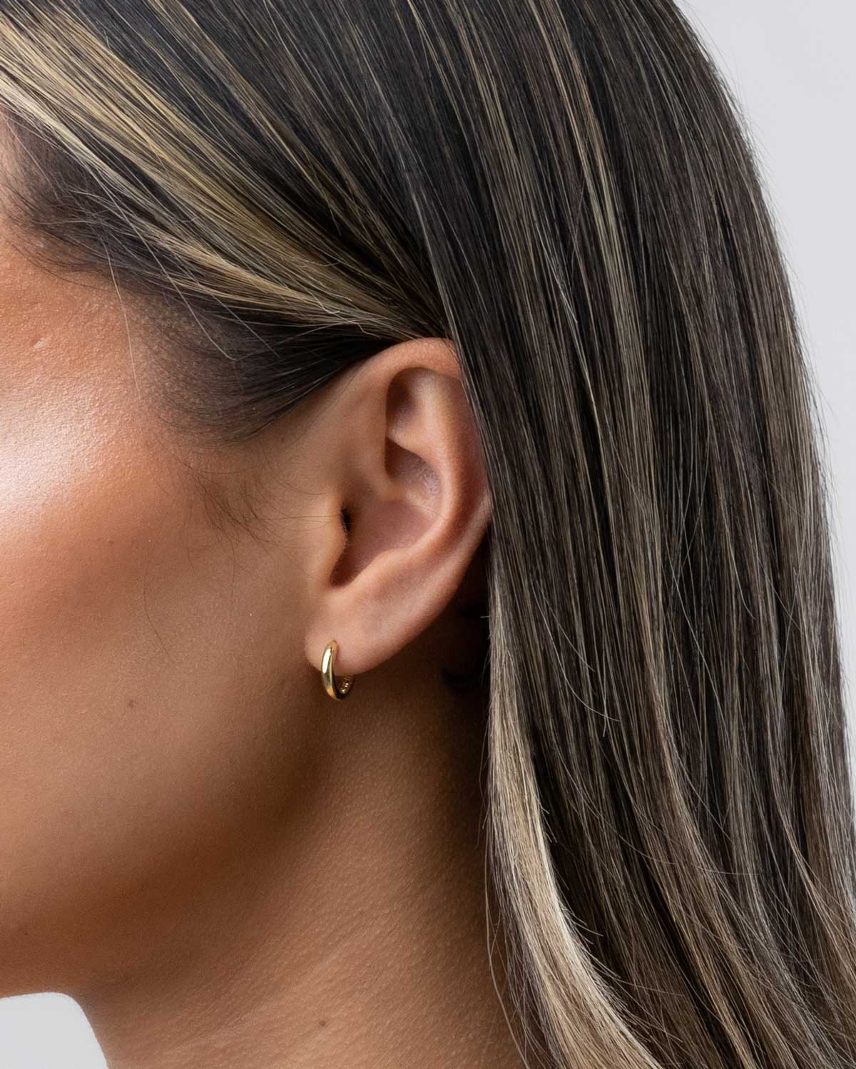 18 karat yellow gold mini huggies claude by claudia on model close up shot of ear