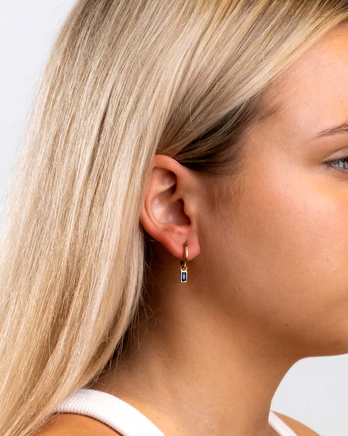 blonde model wearing the 9 karat yellow gold with sapphire drop charms by claude and me jewellery.