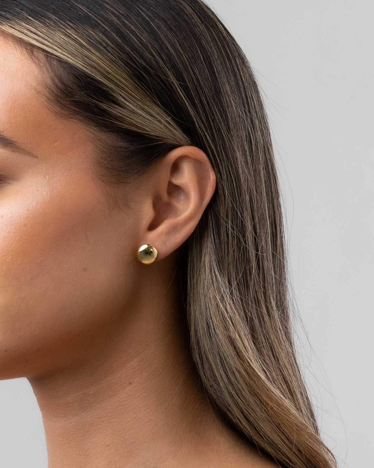 Claude by Claudia button studs in 18 karat yellow gold featured in female models ear.