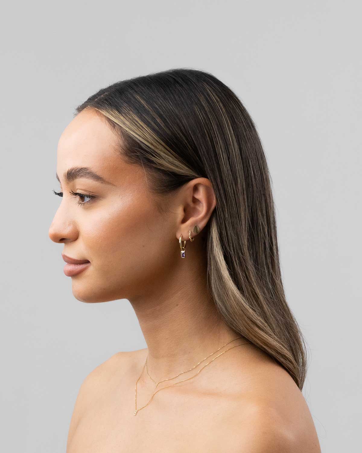 Model imagery of 9 karat yellow gold charm hoop earrings with amethyst bezel set drops from the claude by Claudia collection.