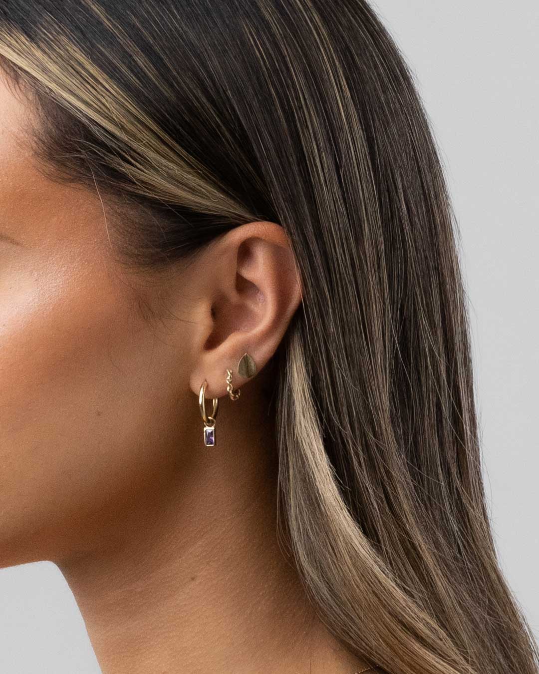 Close up earring imagery of 9 karat yellow gold charm hoop earrings with amethyst bezel set drops from the claude by Claudia collection.