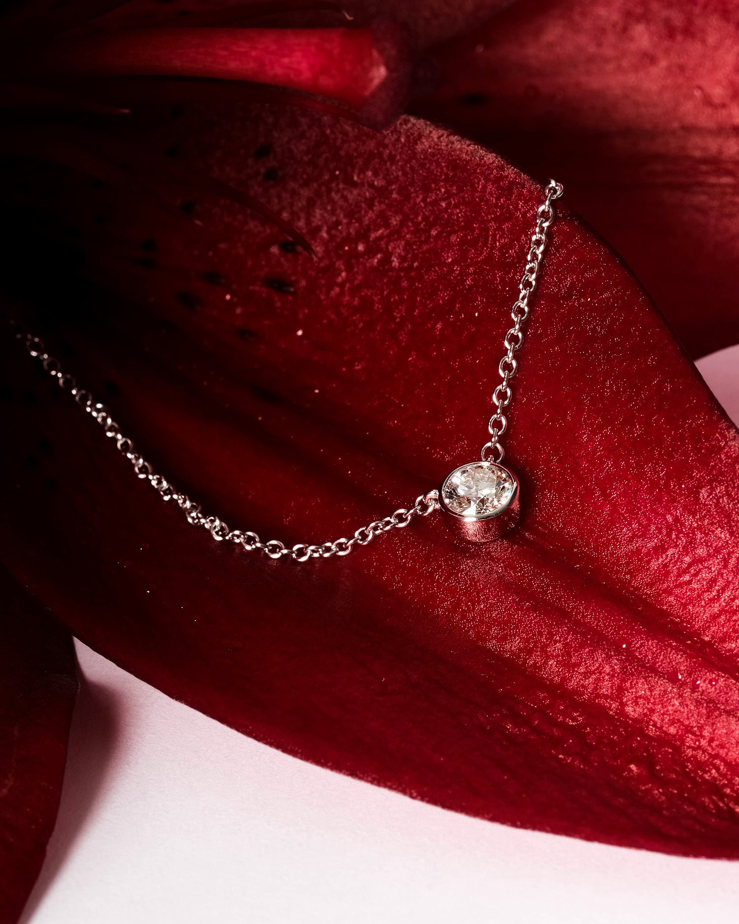 close up of diamond bezel set pendant resting on red lillie flower