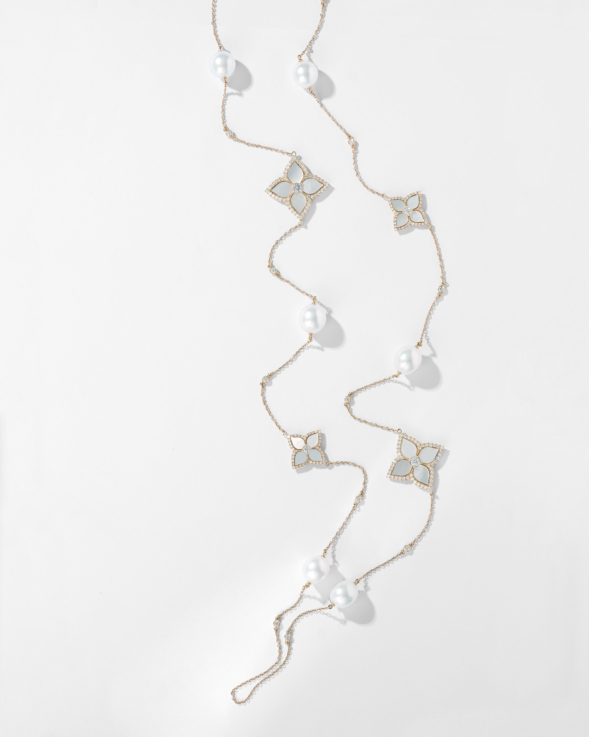 18k yellow gold opera length necklace with four mother of pearl floral motifs outlined in pavé diamonds and six round white Australian South Sea pearls along a diamond station chain, photographed on a white background.